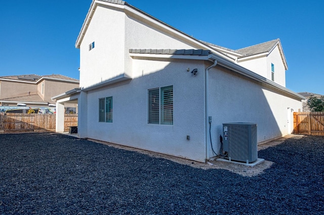 rear view of house with cooling unit, stucco siding, and fence