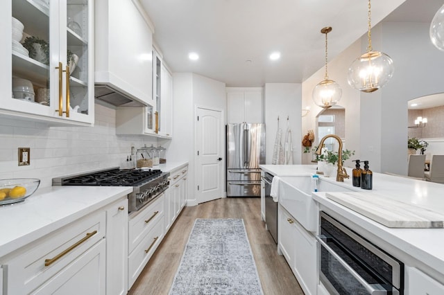 kitchen featuring appliances with stainless steel finishes, a sink, custom range hood, tasteful backsplash, and light wood-type flooring