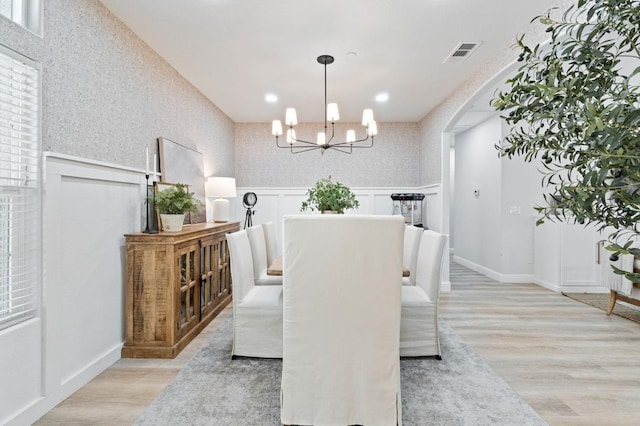 dining room with light wood-style flooring, an inviting chandelier, visible vents, a decorative wall, and arched walkways