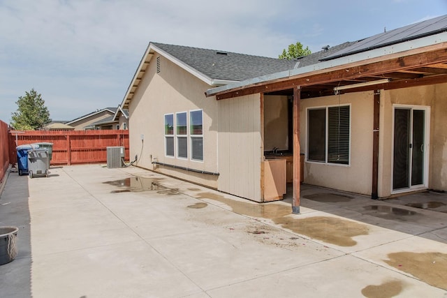 rear view of property with central air condition unit, a patio area, roof with shingles, and fence
