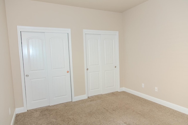 unfurnished bedroom featuring baseboards, multiple closets, and carpet