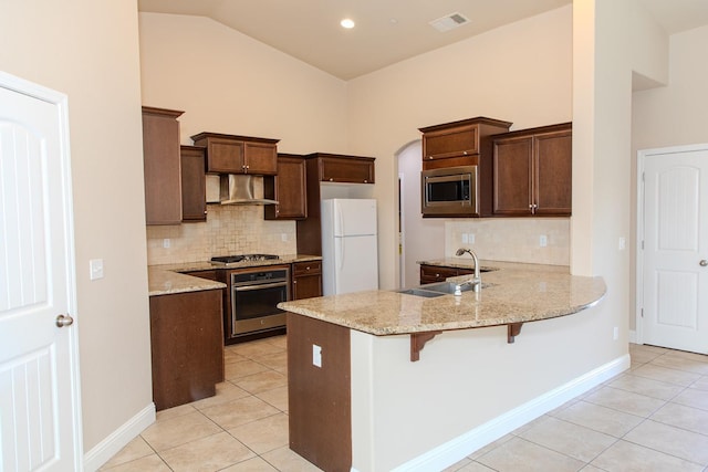 kitchen with a peninsula, wall chimney range hood, light tile patterned floors, and appliances with stainless steel finishes
