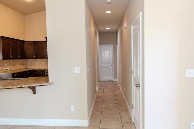 hallway with baseboards, recessed lighting, light tile patterned flooring, and a sink