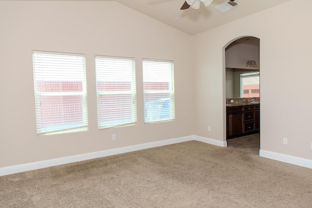 spare room with light colored carpet, visible vents, vaulted ceiling, a ceiling fan, and baseboards