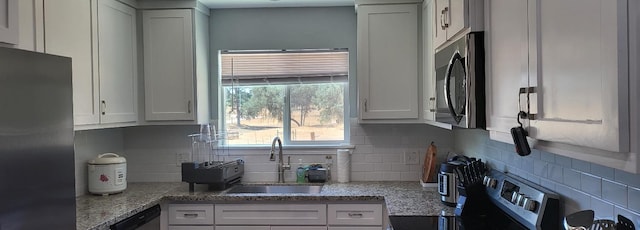 kitchen featuring a sink, stainless steel appliances, white cabinetry, light stone countertops, and tasteful backsplash