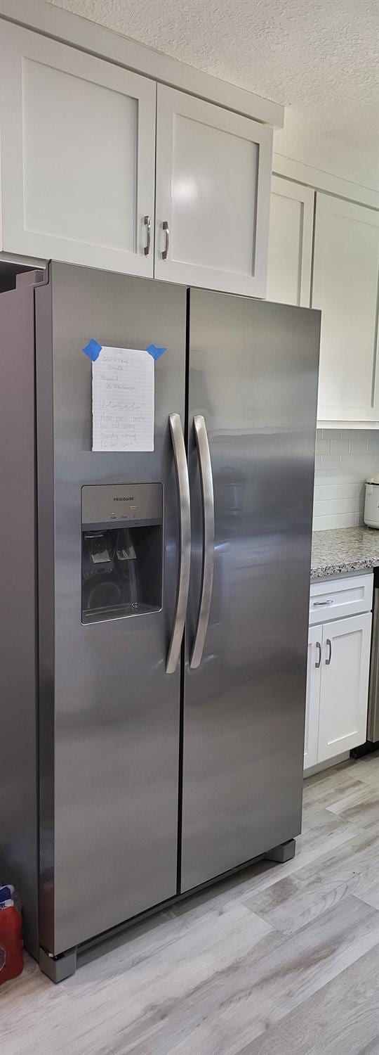 interior details with tasteful backsplash, light stone counters, light wood-style flooring, white cabinetry, and stainless steel fridge