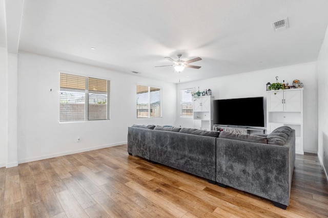 living room featuring light wood-type flooring, visible vents, baseboards, and a ceiling fan