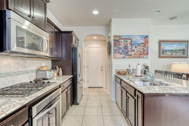 1525 N Piccadilly Ln, Clovis, CA 93619 - kitchen with stainless steel appliances, light stone counters, dark brown cabinetry, backsplash, and arched walkways