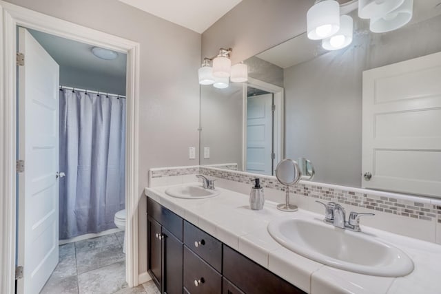 full bath with toilet, tasteful backsplash, double vanity, and a sink