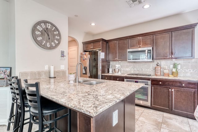 kitchen with a peninsula, dark brown cabinets, a sink, stainless steel appliances, and arched walkways