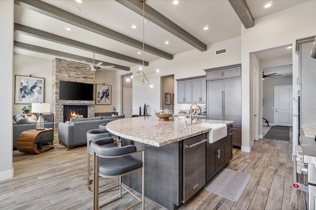 kitchen featuring ceiling fan, a sink, beamed ceiling, a center island with sink, and light stone counters