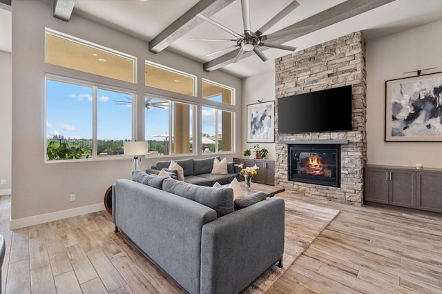 living area with light wood finished floors, ceiling fan, beam ceiling, a stone fireplace, and baseboards