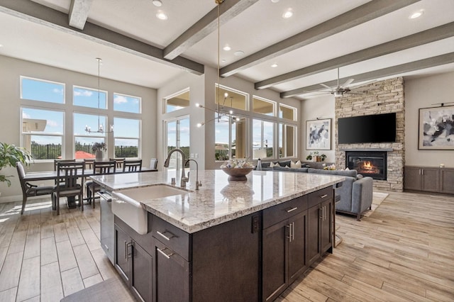kitchen featuring a sink, light wood-style flooring, a fireplace, beam ceiling, and dark brown cabinets