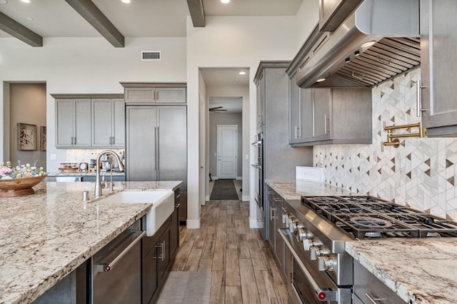 kitchen with range hood, a sink, beamed ceiling, dishwasher, and light stone countertops