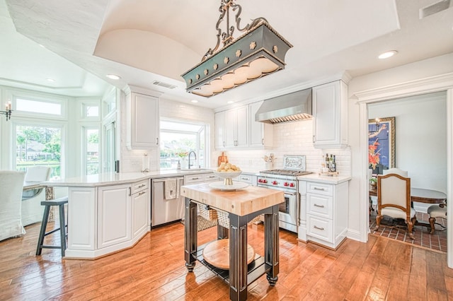 kitchen featuring a peninsula, a sink, wall chimney exhaust hood, visible vents, and appliances with stainless steel finishes