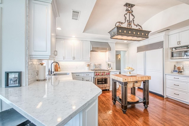 kitchen featuring a sink, wall chimney range hood, visible vents, high quality appliances, and white cabinets