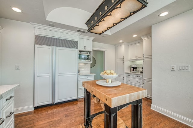 kitchen with white cabinets, visible vents, built in appliances, light countertops, and tasteful backsplash