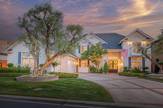 traditional-style home featuring a yard, concrete driveway, a garage, and french doors