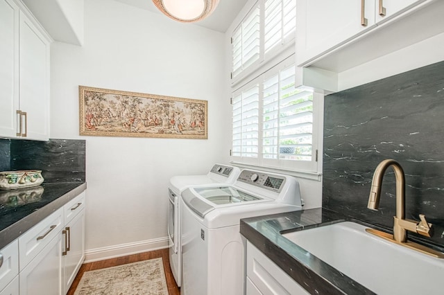 washroom with a sink, washer and clothes dryer, cabinet space, wood finished floors, and baseboards