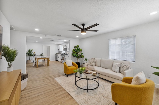 living room featuring ceiling fan, a textured ceiling, light wood-type flooring, and recessed lighting