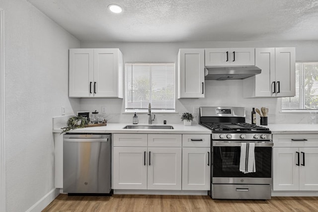 2194 N Feland, Fresno, CA 93722 - kitchen featuring stainless steel appliances, under cabinet range hood, a sink, light wood-style flooring, and a textured ceiling