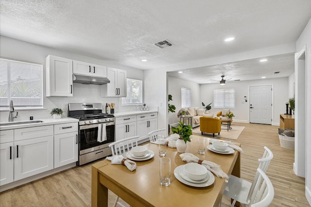 kitchen featuring a sink, under cabinet range hood, light countertops, a ceiling fan, and stainless steel gas range