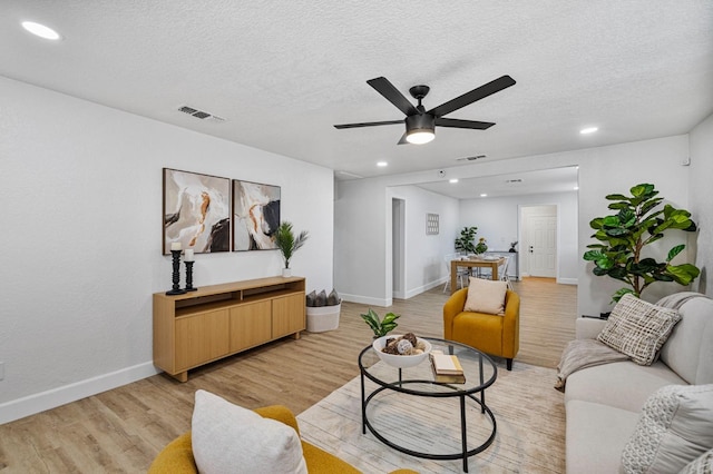 living room with light wood-type flooring, a ceiling fan, visible vents, and recessed lighting