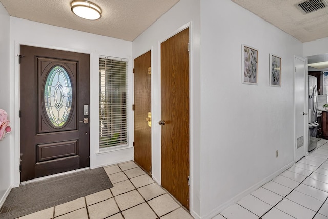foyer featuring a textured ceiling, light tile patterned floors, and baseboards
