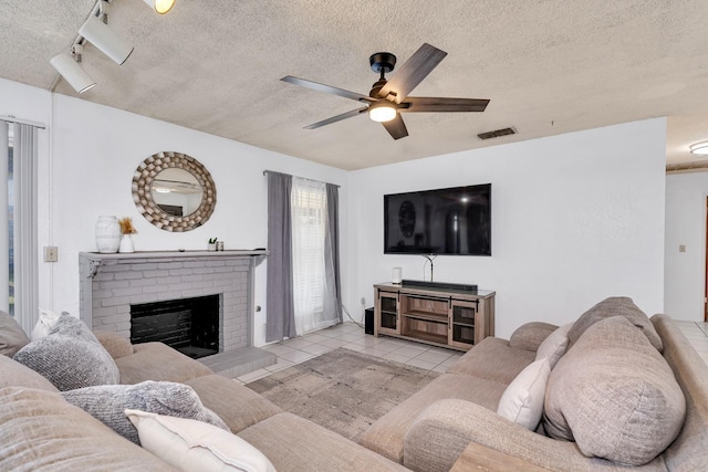 tiled living room featuring a ceiling fan, a textured ceiling, and a brick fireplace