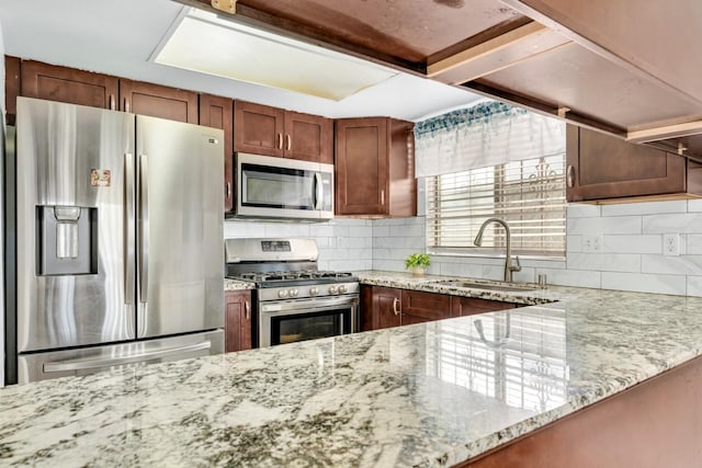 kitchen with stainless steel appliances, a sink, light stone countertops, backsplash, and brown cabinets