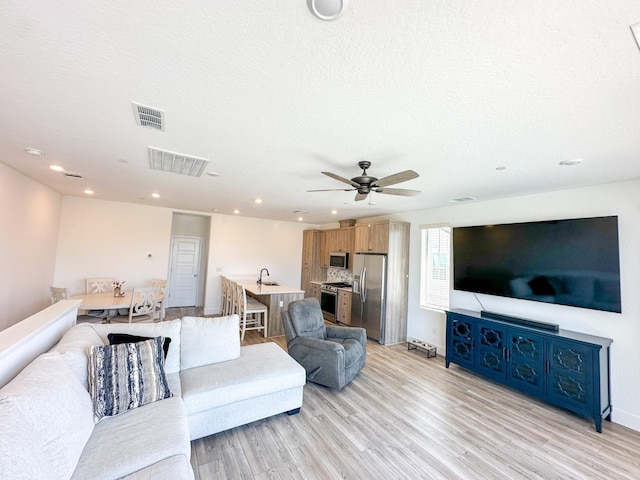 living room with light wood finished floors, recessed lighting, a ceiling fan, and a textured ceiling