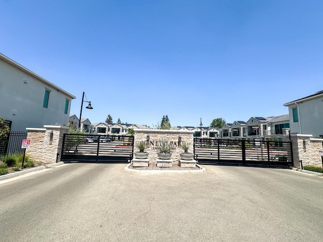 view of asphalt street with a gate, a gated entry, and a residential view