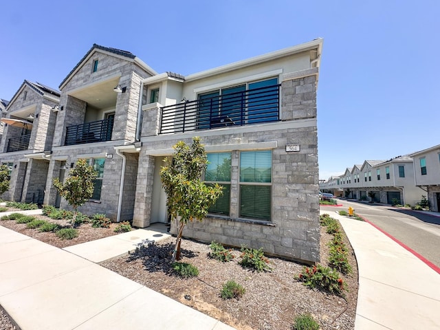 view of front of property featuring stone siding, a balcony, and stucco siding