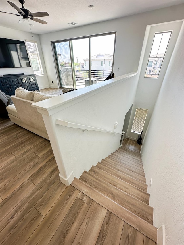 stairway featuring wood finished floors, ceiling fan, and baseboards