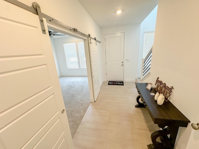 hall with a barn door, light tile patterned flooring, light carpet, and baseboards
