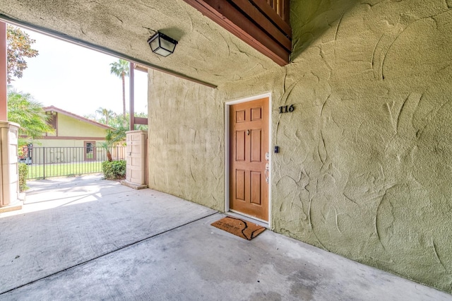 view of exterior entry featuring stucco siding, fence, and a patio area
