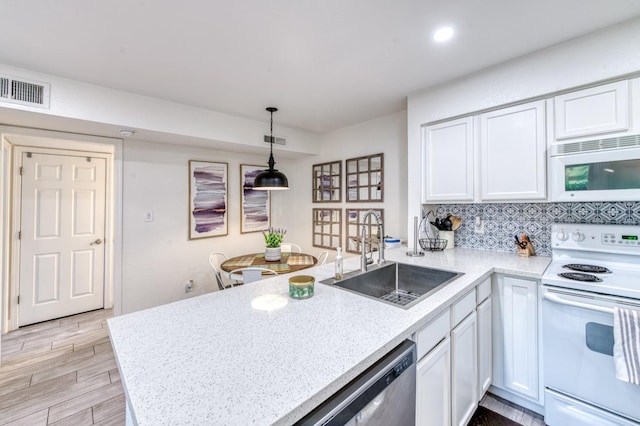 kitchen featuring white appliances, a sink, a peninsula, white cabinetry, and decorative light fixtures