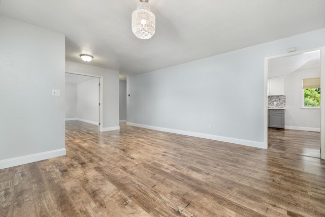 unfurnished living room with wood finished floors, baseboards, and a chandelier