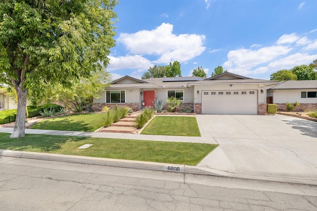 view of front of home with an attached garage, roof mounted solar panels, a front yard, driveway, and stucco siding