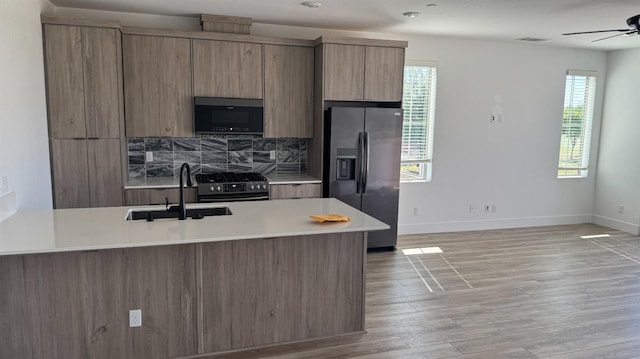kitchen with appliances with stainless steel finishes, a sink, light countertops, ceiling fan, and tasteful backsplash