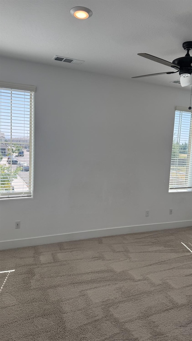 carpeted empty room featuring ceiling fan, baseboards, and plenty of natural light