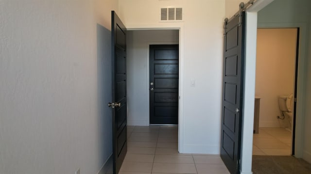 corridor featuring light tile patterned floors, baseboards, and a barn door
