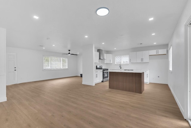 424 W Menlo Ave, Clovis, CA 93612 - kitchen with stainless steel gas stove, wall chimney exhaust hood, open floor plan, a kitchen island, and white cabinets
