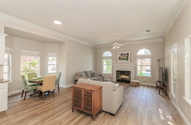 living room featuring light wood-style floors, ceiling fan, a brick fireplace, baseboards, and ornamental molding