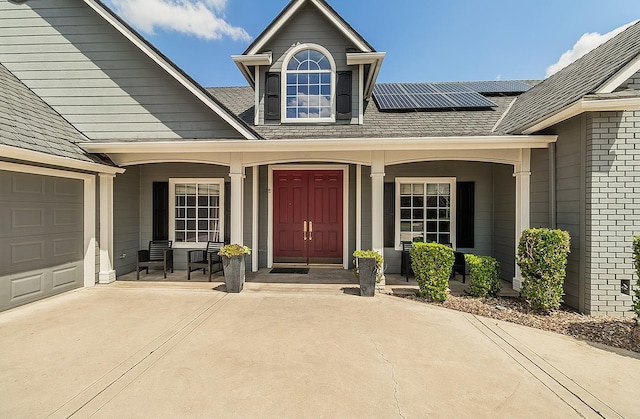 property entrance featuring covered porch, roof mounted solar panels, concrete driveway, and an attached garage