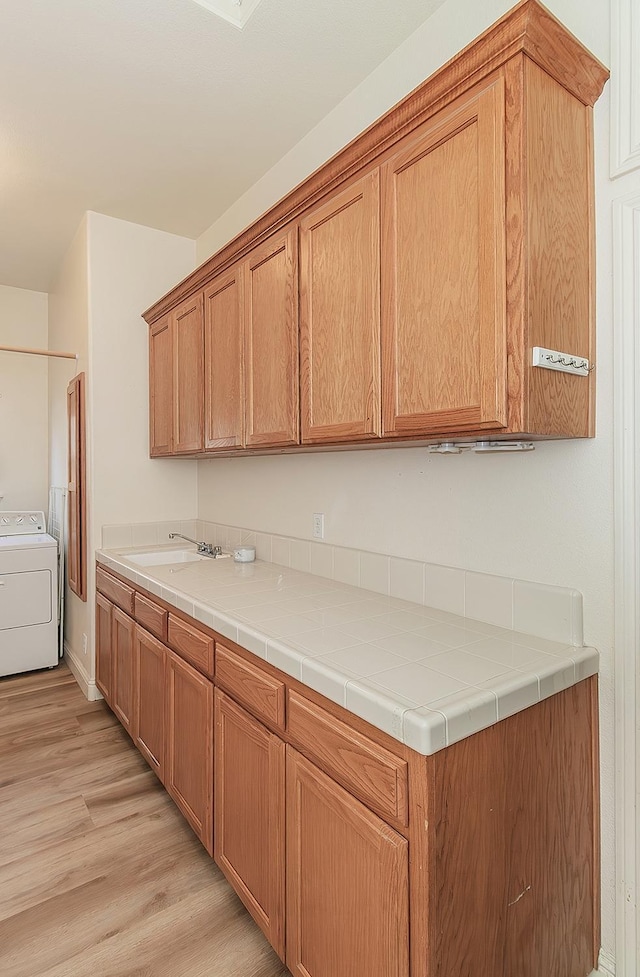 kitchen with washer / dryer, light wood finished floors, a sink, and light countertops