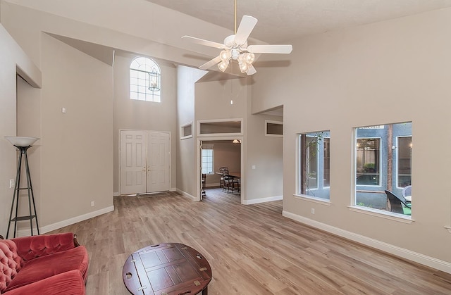 living room with a high ceiling, light wood-type flooring, baseboards, and ceiling fan