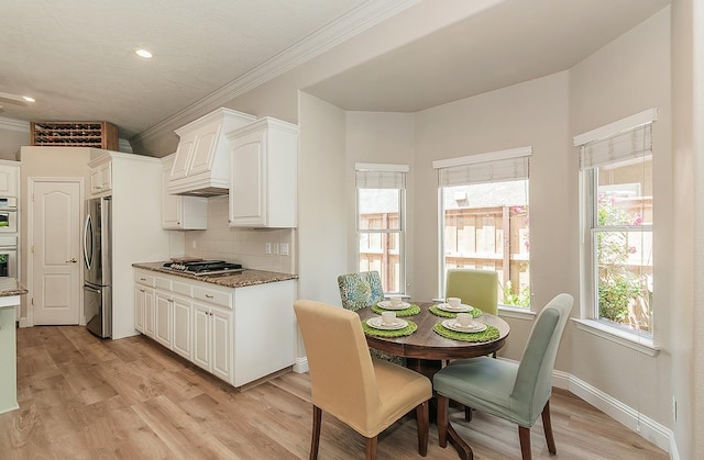 kitchen featuring stainless steel appliances, light stone counters, crown molding, tasteful backsplash, and white cabinetry