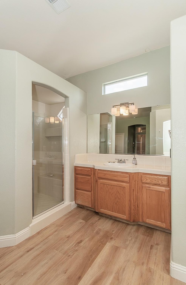 bathroom featuring wood finished floors, a shower stall, vanity, and baseboards