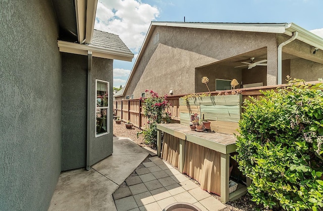 view of home's exterior with stucco siding, a ceiling fan, and fence